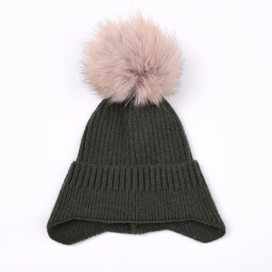 Detail of dark green ribbed knit beanie with a large pink faux fur pompom and ear flaps