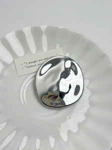 Macro shot of silver irregular round brooch with mirror finish on white plate