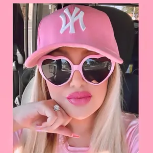 Pink heart-shaped polarized sunglasses for women styled with an embroidered baseball cap