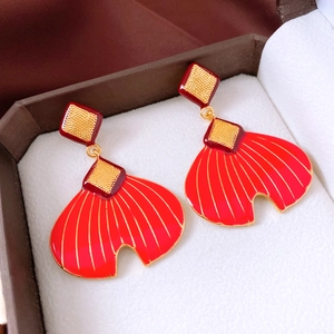 Macro shot of red enamel fishtail fan earrings with gold-plated accents in a box