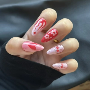 Macro view of long almond press-on nails with red heart, cherry, and flame patterns
