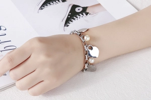 Détail d'un bracelet à breloques cœur argenté avec perles blanches sur poignet