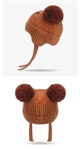 Detail view of baby knit hat with double brown pom poms and warm ear flaps design