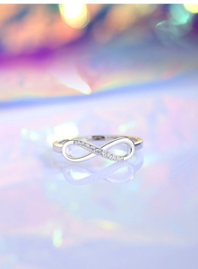 Macro shot of silver infinity ring with white crystals on a reflective surface