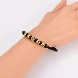 Braided leather bracelet with gold beads and a black gemstone center on a model wrist