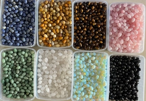 Top-down view of eight transparent boxes filled with assorted egg-shaped natural stone crystals