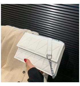 Close-up of a white quilted crossbody bag featuring a silver chain strap and geometric texture