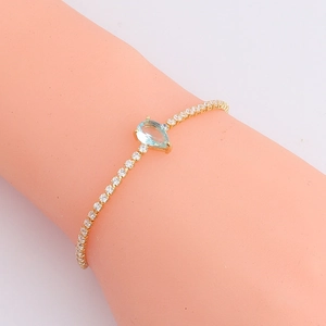 Detail of gold-plated bracelet with pavé cubic zirconia and a pear-cut blue centerpiece
