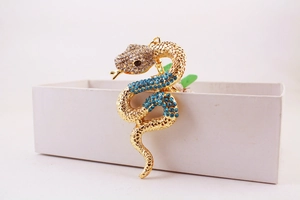 Detailed shot of a gold snake keychain with blue rhinestones leaning on a white gift box