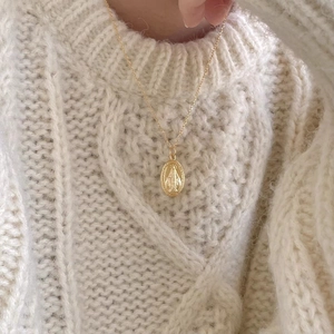 Detail of a vintage 925 sterling silver Virgin Mary medallion necklace on a knit sweater