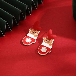 Detailed shot of Christmas bear and snowflake glove earrings on red festive background