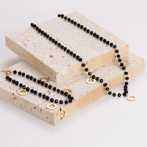 Elegant black glass bead necklace and bracelet set with round gold pendant on stone base