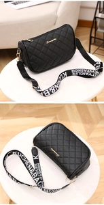 Detail view of black quilted crossbody bag with gold hardware and wide lettered strap