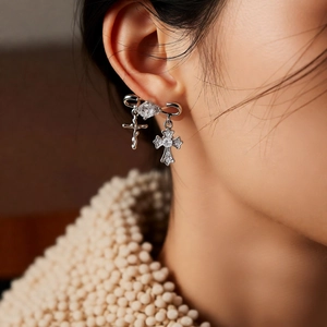 Close-up of silver bow and cross drop earrings worn by a model in a trendy style