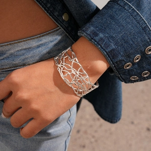 Close-up of a silver hollow crisscross cuff bracelet worn with a stylish denim jacket