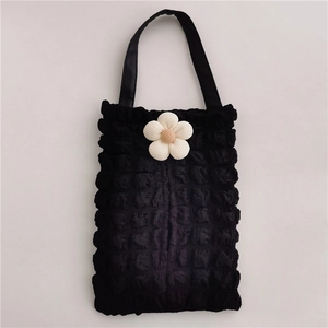 Detailed top view of black popcorn textured tote bag with a white floral accent