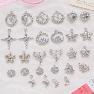 Flat lay of silver charms with star, bow, and cross designs on soft white fabric