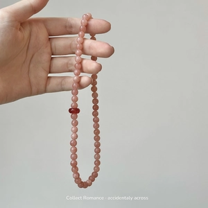 Handheld view of translucent orange-pink natural stone beaded bracelet with red accent bead