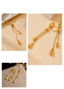 Detail of golden teardrop pendant necklace and earrings set on a textured stone surface