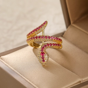Detail of a gold snake ring with red and white zircons inside a beige jewelry box