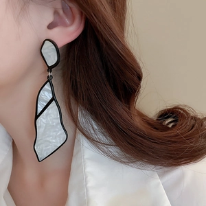 Close-up of geometric black-edged pearl textured earrings worn by a model