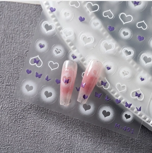 Detailed view of white heart and purple butterfly nail stickers on matte textured nails