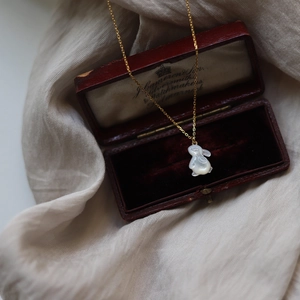 Détail du pendentif lapin en nacre blanche sur chaîne dorée et boîte à bijoux vintage
