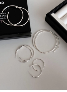 Detailed view of four pairs of polished silver hoop earrings in varying sizes on a tray