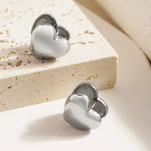 Elegant polished silver heart stud earrings for women on a beige stone background