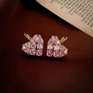 Boucles d'oreilles cœur dorées avec zircons roses sur un fond de style vintage