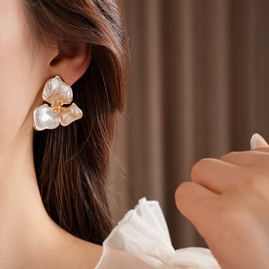Detail of white shell flower earring with gold pistil worn by a model in soft light