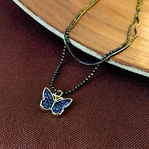 Close-up of double-layer necklace with blue crystal butterfly pendant and golden snake chain