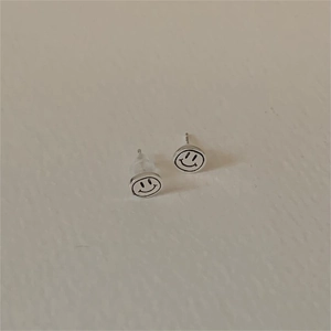 Minimalist 925 sterling silver smiley face stud earrings on a beige background