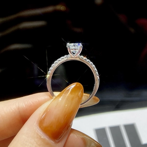 Close-up of a pink four-prong silver ring with central moissanite stone and side diamonds