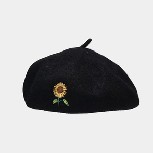 Close-up of sunflower embroidery detail on a black wool beret with sharp fabric texture