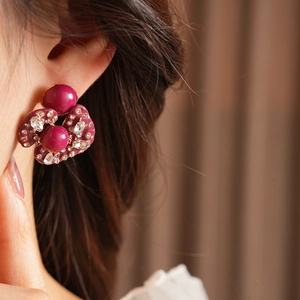 Close-up of irregular burgundy vintage stud earrings with inlaid crystals on a model