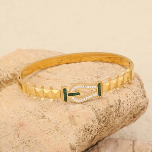 Golden butterfly heart bracelet with green inlay and crystals on a stone background