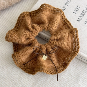 Close-up of brown knit scrunchie with a small bow and gold metal charm on soft fabric