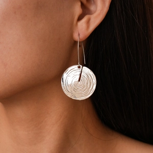 Close-up of silver geometric spiral textured metal hoop earring on model