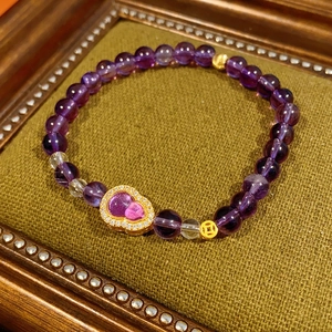 Detailed close-up of purple beaded bracelet with golden gourd charm on velvet tray