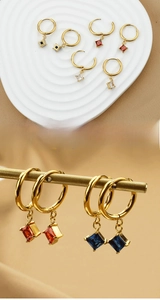 Detailed macro view of gold hoop earrings with square red zircon pendants and clear stones