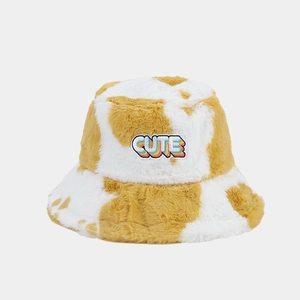 Détail d'un bob en peluche motif vache jaune et blanc avec écusson brodé CUTE
