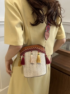 Detail of woven straw bucket bag with colorful tassels and geometric patterned strap