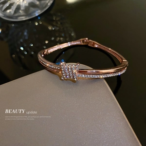 Elegant rose gold knot bangle with sparkling cubic zirconia on a minimalist grey pedestal