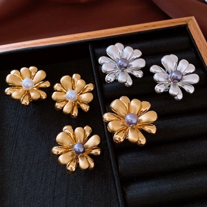 Detailed top view of flower pearl earrings in gold and silver finish on black velvet