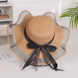 Detail of a brown straw hat with a wavy brim, black lace trim, and a branded bow ribbon