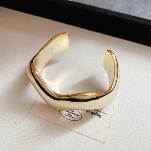 Macro del bracciale rigido dorato a onde irregolari su tessuto minimalista