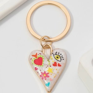 Détail d'un porte-clés cœur blanc avec motifs graffiti colorés et anneau en métal doré