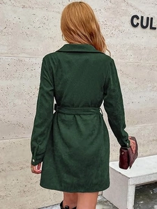 Back view of dark green corduroy shirt dress with waist belt against grey wall