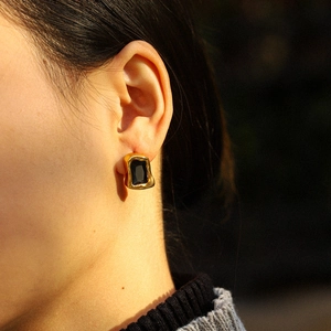 Detail of vintage gold-framed black rectangular earring worn by a model in warm light